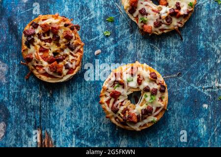 Top down close up view of three homemade pizza bagels against. a blue background. Stock Photo