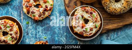 Top down narrow view of homemade everything pizza bagels on a wooden board and against a blue background. Stock Photo