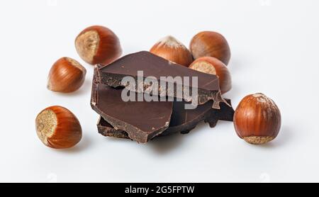 Ripe wild hazelnuts and bitter chocolate. Nuts and and stack of a dark chocolate on a white background. Natural organic products. Copy space. Food ban Stock Photo