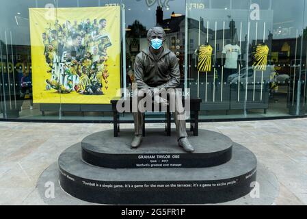 Watford, UK.  27 June 2021.  A statue of former manager Graham Taylor wearing a facemask outside a pop-up mass vaccination clinic at Watford FC’s Vicarage Road Stadium as part of the “Grab a jab” campaign. The NHS is also promoting a number of walk-in clinics this weekend across the capital to try to increase the number of over 18s receiving a jab as cases of the Delta variant are reported to be on the rise.  Credit: Stephen Chung / Alamy Live News Stock Photo