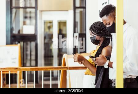 Two african students with mask using their mobile phones on campus Stock Photo
