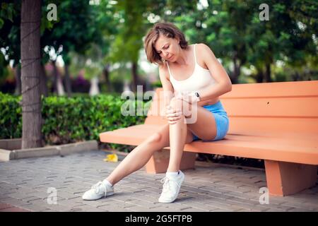 Knee pain. Woman with knee injury sitting on the bench outdoor. Healthcare and lifestyle concept Stock Photo