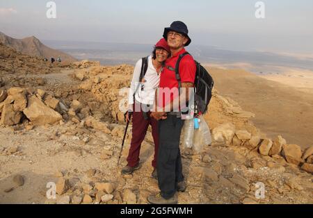 Married man & woman hikers, senior adults, she leans on his shoulders, they both smile to the camera, Nachal Rahaf, Judean Desert & Rift Valley behind Stock Photo