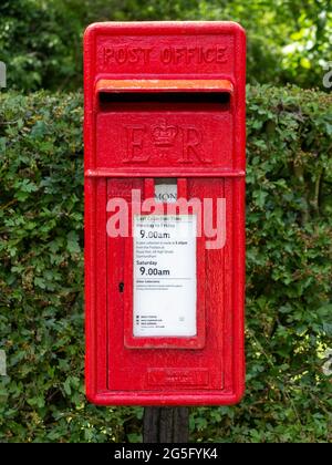 Red cast iron Post Office letter box mounted on a post in front of a hedge Stock Photo
