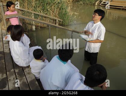 Korean Protestant youth wear white gowns listen to the pastor read the Bible before baptising in the Jordan River in Qasr El Yahud where Christ did. Stock Photo