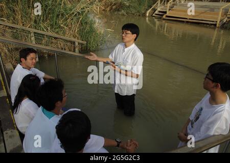 Korean Protestant youth wear white gowns listen to the pastor read the Bible before baptising in the Jordan River in Qasr El Yahud where Christ did. Stock Photo