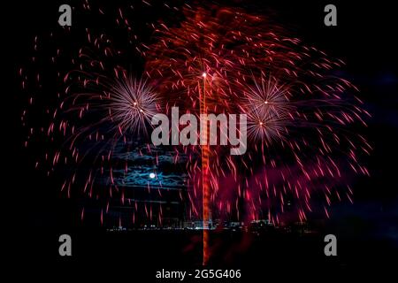 Red fireworks fill the night sky, raining down sparks of color over Parliament Hill. The full moon illuminating the clouds completes the scene. Stock Photo