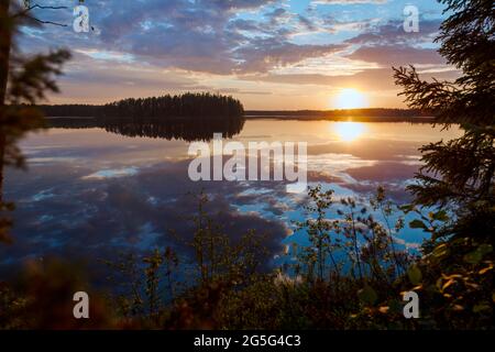 Scenic and beautiful sunset and dramatic cloudy sky and their reflections on a calm lake in Finland at summer. Stock Photo