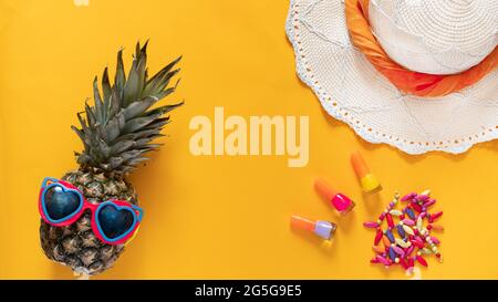 Summer composition. Pineapple in sunglasses, hat, beads and nail polishes on a yellow background with copy space. Vacation concept. Flat lay. Stock Photo