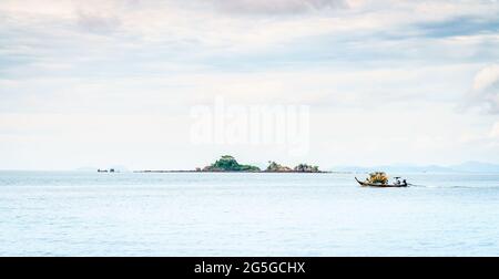 Thai long tail boat speeding past an island off Krabi coast in the Andaman Sea, Thailand Stock Photo