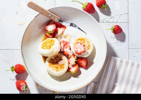 Homemade cottage cheese fritters - syrniki with strawberries and sour cream, Russian and Ukrainian cuisine concept. Stock Photo