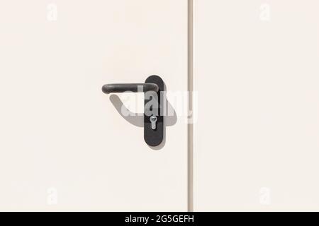 Light pastel colored metal door with lock and black handle close-up. Stock Photo