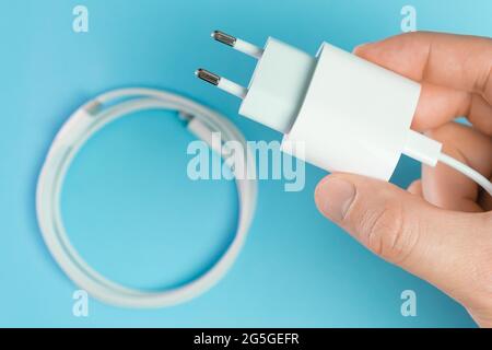 A white smart phone charger cable with lightning hi speed USB type C connector and adapter in man hand on the blue background. Stock Photo