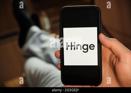 Hinge logo on the screen of smartphone in mans hand laying on the sofa. Application for dating, June 2021, San Francisco, USA Stock Photo