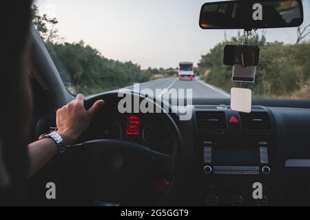 man holding steering wheel with one hand drives on empty road. Driving with one hand is dangerous. Stock Photo