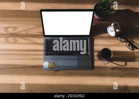 BTC coin, laptop and a glass of coffee stand on the table in the morning when the day is lit up. Stock Photo