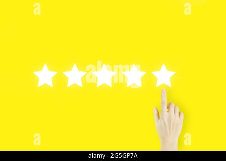 Increase rating evaluation and classification concept. Customer Experience Concept. Young woman's hand finger pointing with hologram Five stars on yel Stock Photo