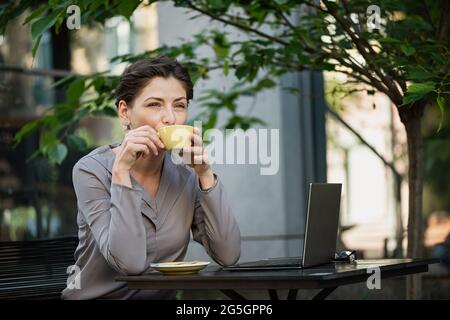 Beautiful business woman is drinking coffee at a table in an outdoor restaurant. Stock Photo