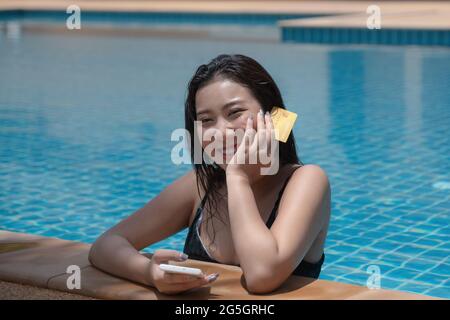 Young woman with bikini in pool using smartphone and holding credit card for shopping online. Everywhere Online shopping concept. Stock Photo