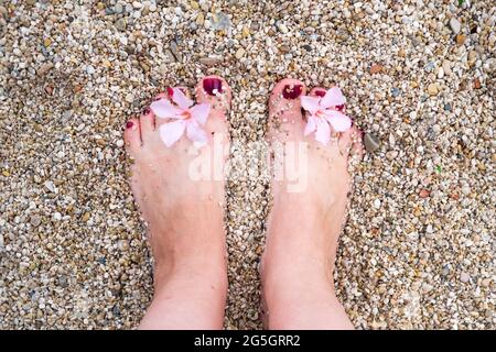 Female foot with a red pedicure on a pebble beach by the sea. Stones on a feet. Snapshot style photo. Stock Photo