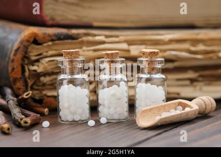 Bottle of homeopathic granules and wooden scoop of white globules. Old books on background. Homeopathy medicine concept. Stock Photo