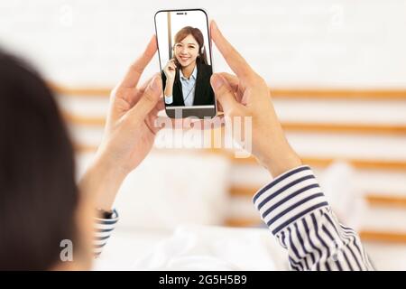young man lying on the bed at home and  having  video call with  business woman Stock Photo