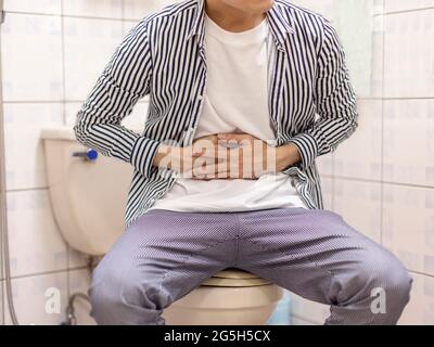 Young man holding his abdomen feels sick and constipation in the toilet Stock Photo