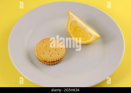 Lemon cream sandwich cookie with lemon slice on white snack plate with yellow background Stock Photo