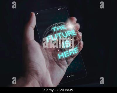 Futuristic modern transparent glass phone technology concept. The future is here, 3d text on the future slim transparent smartphone in hand on dark to Stock Photo