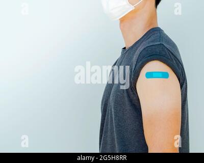 Vaccinations, bandage on vaccinated people concept. Blue bandage on man shoulder who wearing grey shirt and white medical face mask after vaccination Stock Photo