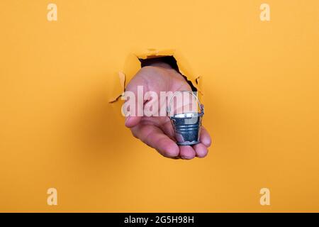 Miniature metal bucket in a woman's hand on a yellow background. Stock Photo
