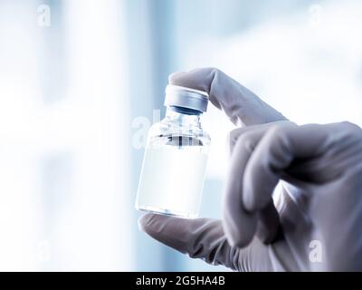 Medical vaccine vial with white blank label in scientist hand with white rubber gloves. Close up image of hand holding vaccine glass bottle for inject Stock Photo