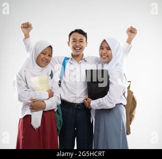 Three teenagers wearing school uniforms smile at the camera with a backpack, a book, and a laptop computer Stock Photo
