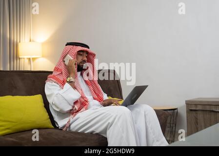an Arab businessman wearing a turban works on a laptop and makes phone calls Stock Photo