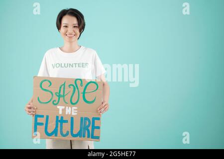 Pretty smiling female volunteer showing save the future placard when attending protest Stock Photo