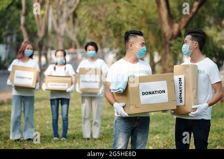 Volunteers in medical masks carrying cordboard boxes and packages filled with donated clotehs and groceries for homeless people