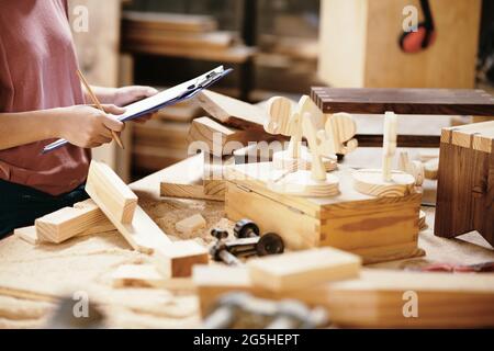 Young woman controlling quality of wooden products that company sells online and taking notes in documant Stock Photo