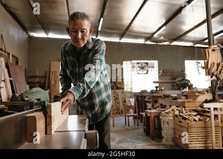 Professional experienced carpenter using bench top jointer to get flat surface along boards length Stock Photo
