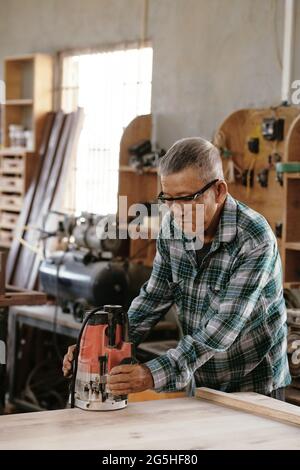 Senior carpenter in goggle sanding wooden board with electric sander Stock Photo