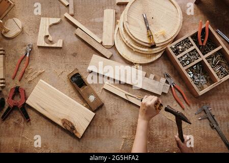 Hands of female carpenter carving wooden pansk with chisel and hammer in workshop, view from tghe top Stock Photo