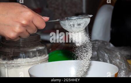 A hand holds a small metal sieve, sifting white blemish into a bowl. Selective focus. Stock Photo