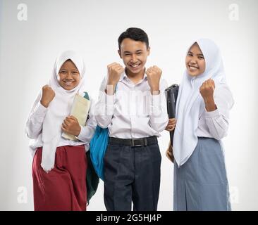 Three teenagers in school uniforms smiled with excited hands gesture when carrying a backpack and a book Stock Photo