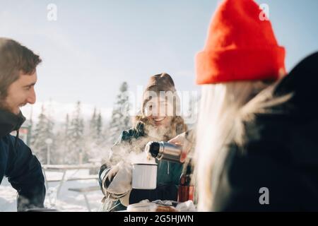 Young woman pouring coffee for female friend during winter Stock Photo