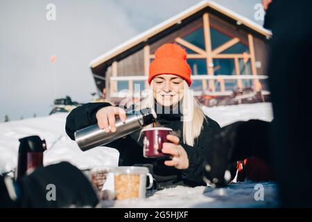 Smiling woman pouring coffee in cup during winter Stock Photo