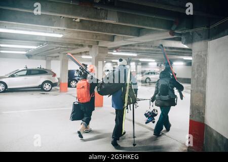 Full length rear view of male and female friends carrying skis while walking at parking garage Stock Photo
