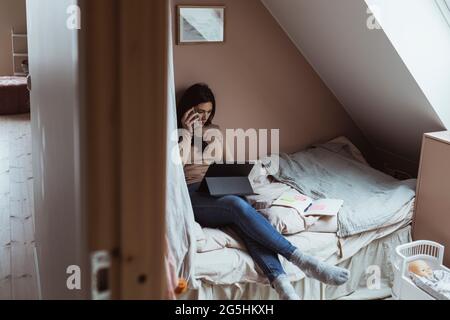 Businesswoman talking on smart phone while using digital tablet in bedroom Stock Photo
