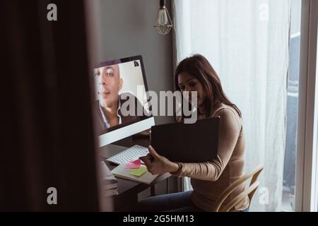 Businesswoman showing laptop to male professional on video call at home office Stock Photo