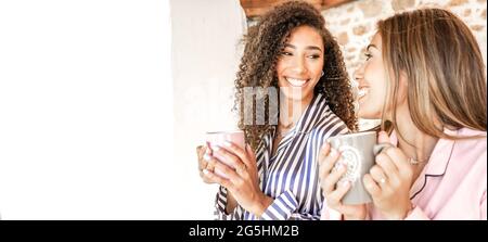 Multiracial women couple smiling looking each other holding a teacup in pajama just waken up. New normal gay families relationship and habits daily li Stock Photo