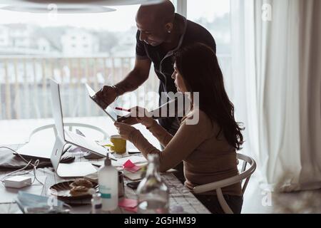 Male and female colleagues discussing over digital tablet at home office Stock Photo