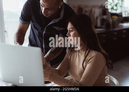 Businesswoman discussing with male colleague over laptop at home Stock Photo